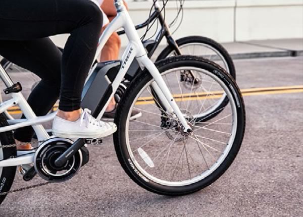 Two people riding bicycles on a road, focusing on the lower halves of their bodies and the bike wheels.