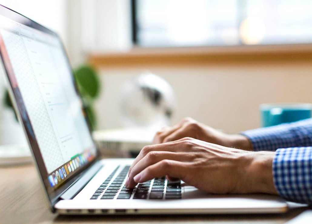 A person's hands typing on a laptop keyboard.