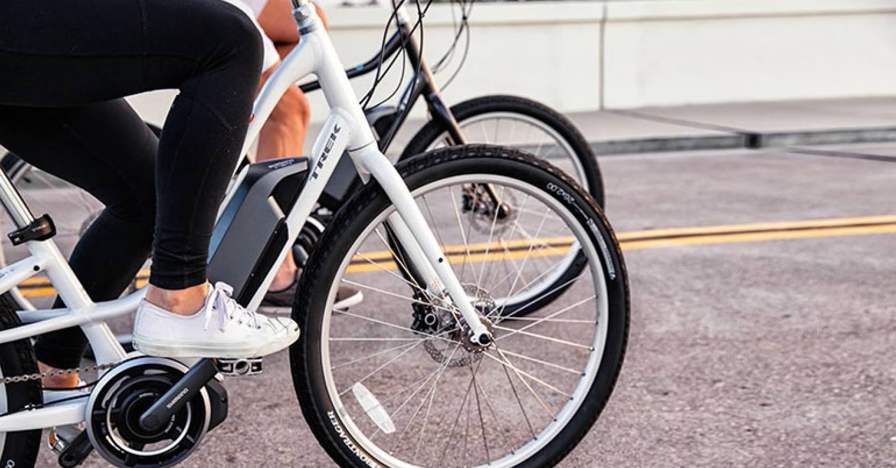 Two people riding bicycles on a road, focusing on the lower halves of their bodies and the bike wheels.