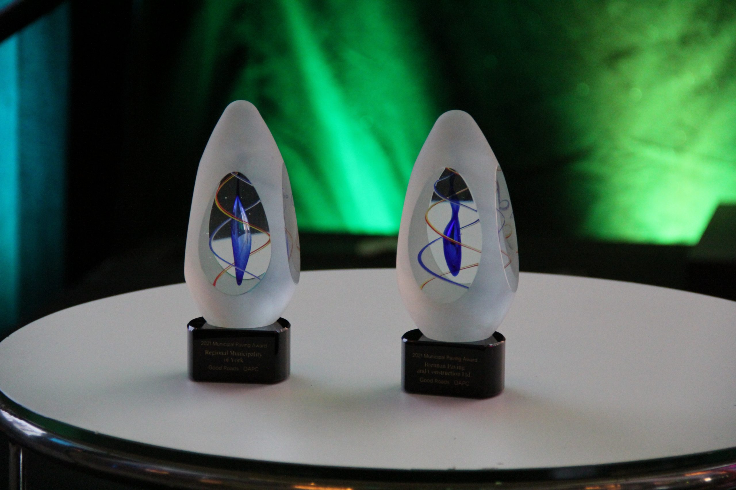 Two glass awards with a blue and colorful design, placed on a round table.