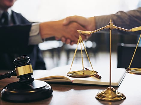 A gavel, scales of justice, and two people shaking hands over a document.