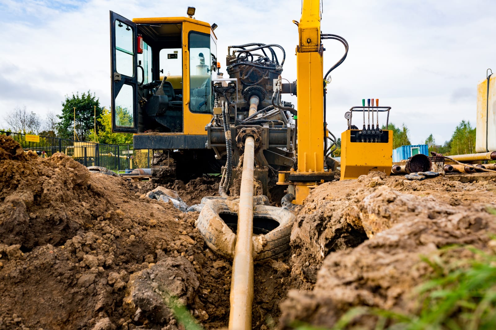 A construction site with a trencher machine digging a trench, surrounded by dirt and grass.