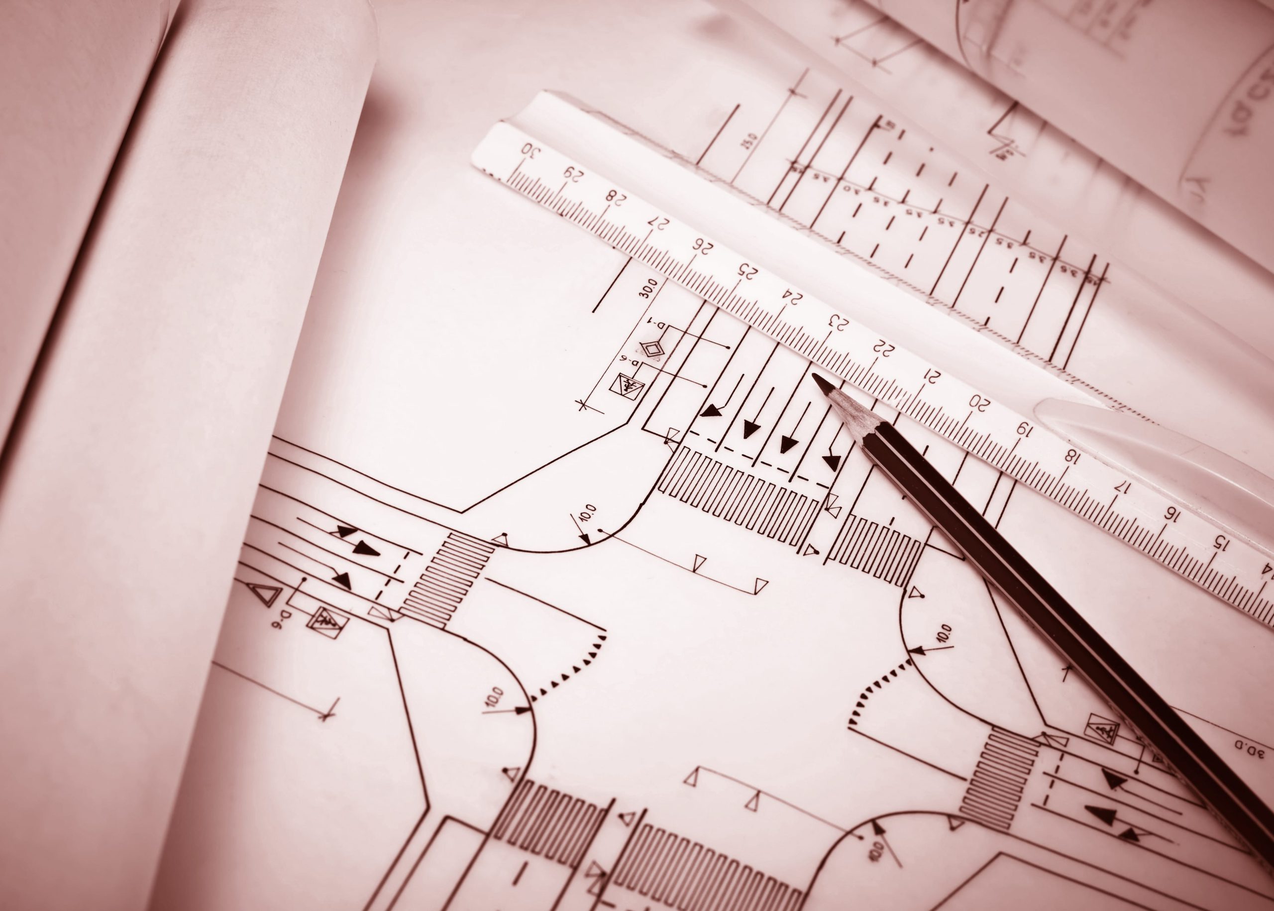 Blueprints of a street layout and drafting tools, including a ruler and pencil, arranged on a table.