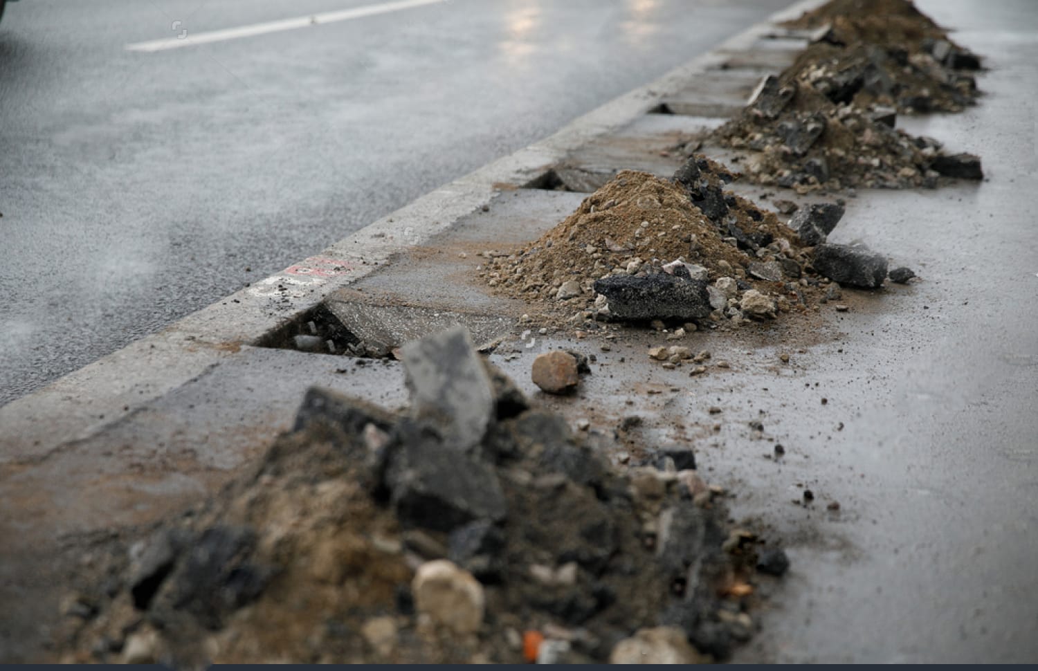 Piles of dirt and debris along a roadside, indicative of construction or roadwork.