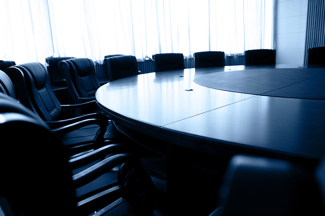 A large, round conference table surrounded by black leather chairs in a well-lit meeting room.