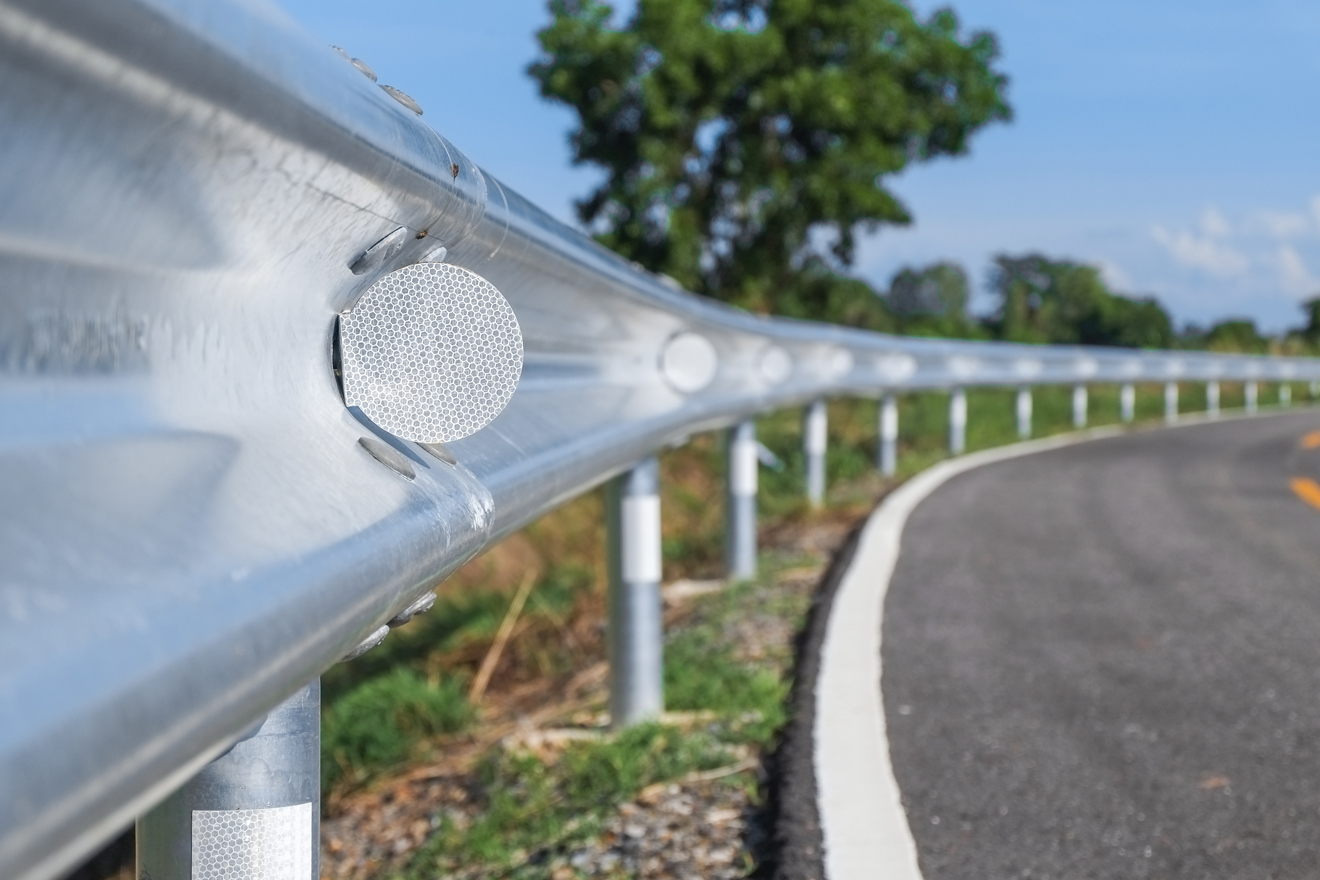 A close-up view of a metal guardrail along a winding road, with trees in the background.