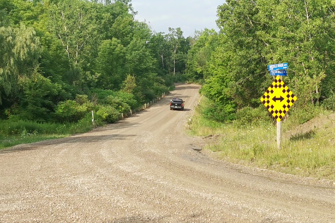 A gravel road surrounded by greenery with a sign indicating a fork in the road.