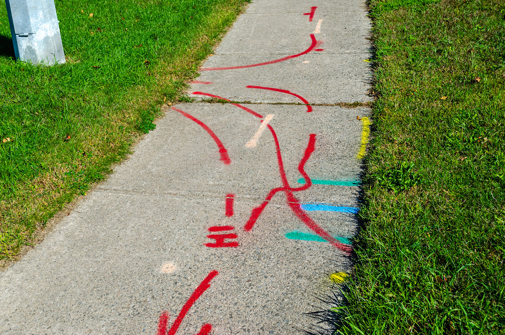 Pattern of hydro, water and gas line markings on a sidewalk next to a metal street light pole,