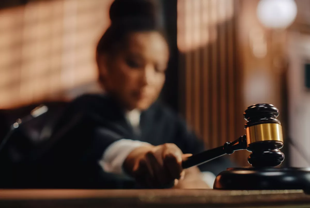 A blurred image of a judge in a courtroom, focusing on a gavel being struck on a sound block.