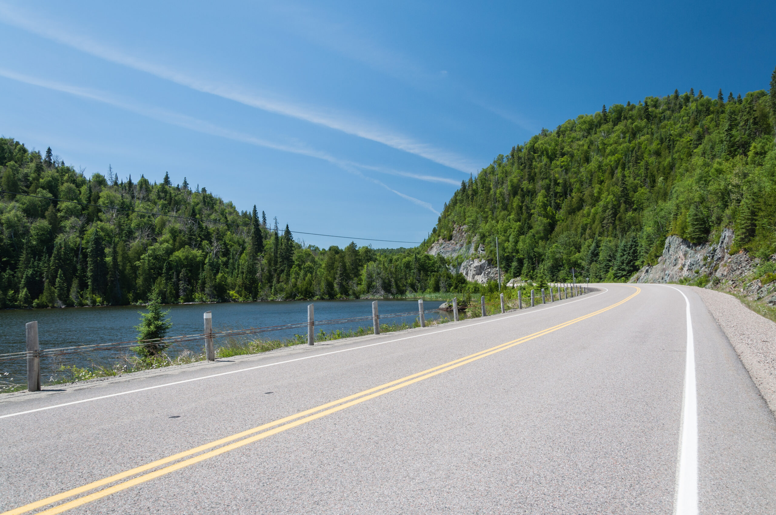 A winding road along a lake with lush green hills and blue sky.