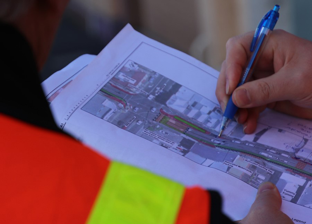 A person in a reflective vest holding a map and a pen, reviewing a street layout.