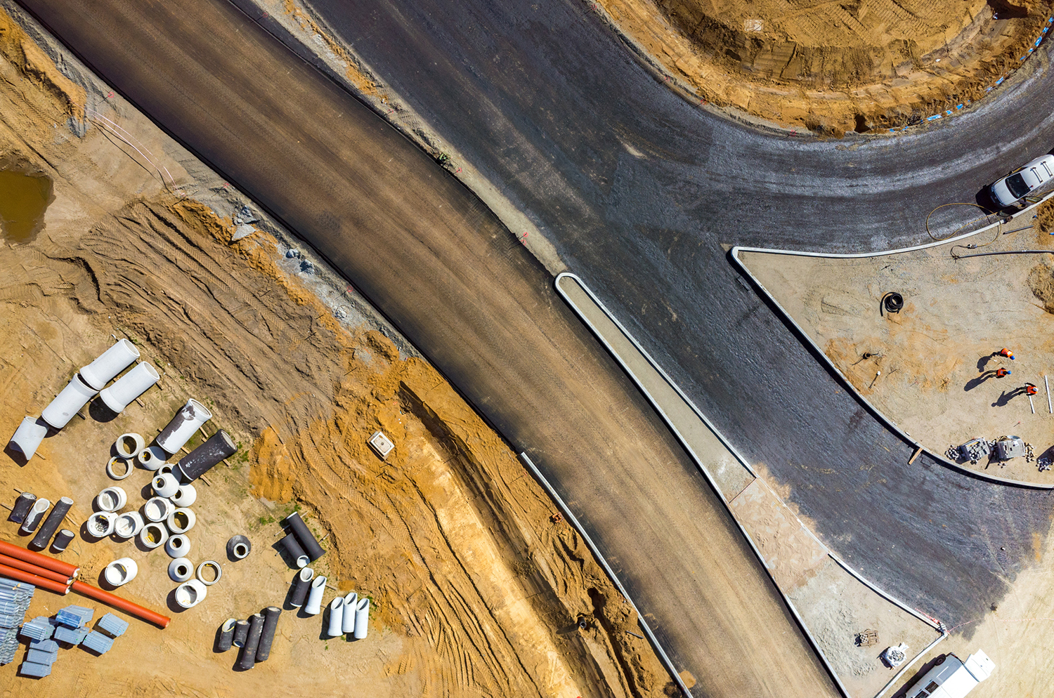 An aerial view of a construction site with freshly paved roads, exposed soil, and construction materials like pipes and concrete.