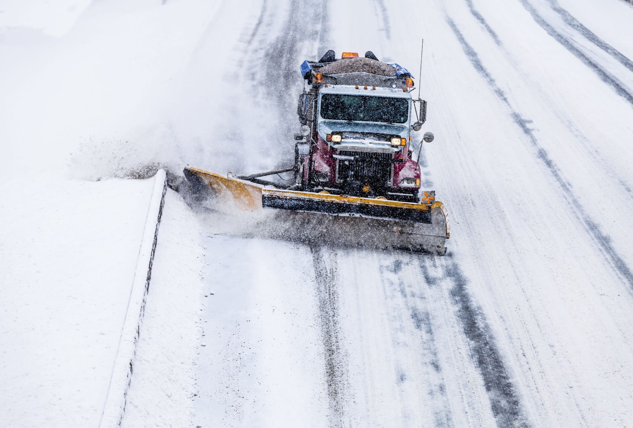 A snow plow clearing a snowy road during a heavy snowfall.