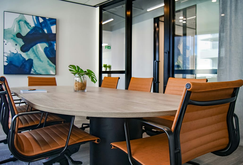 A modern conference room with an oval table, orange chairs, and a large abstract painting on the wall.