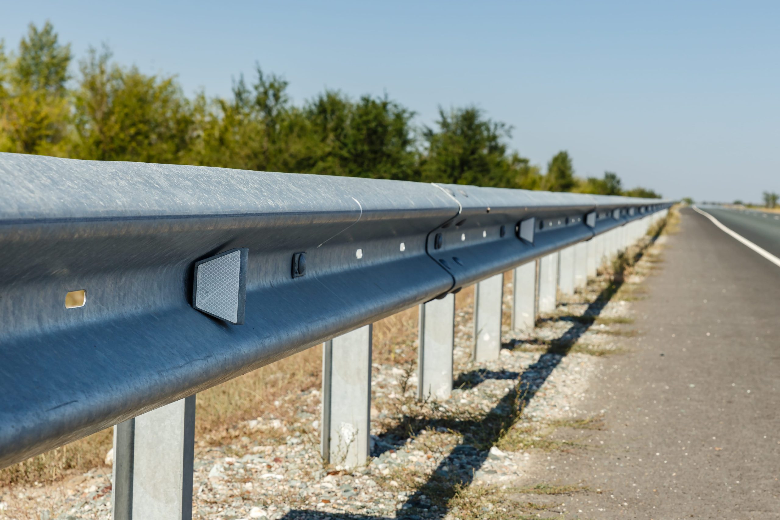 Close-up of a metal guardrail along a highway, with reflective markers and a clear blue sky in the background.