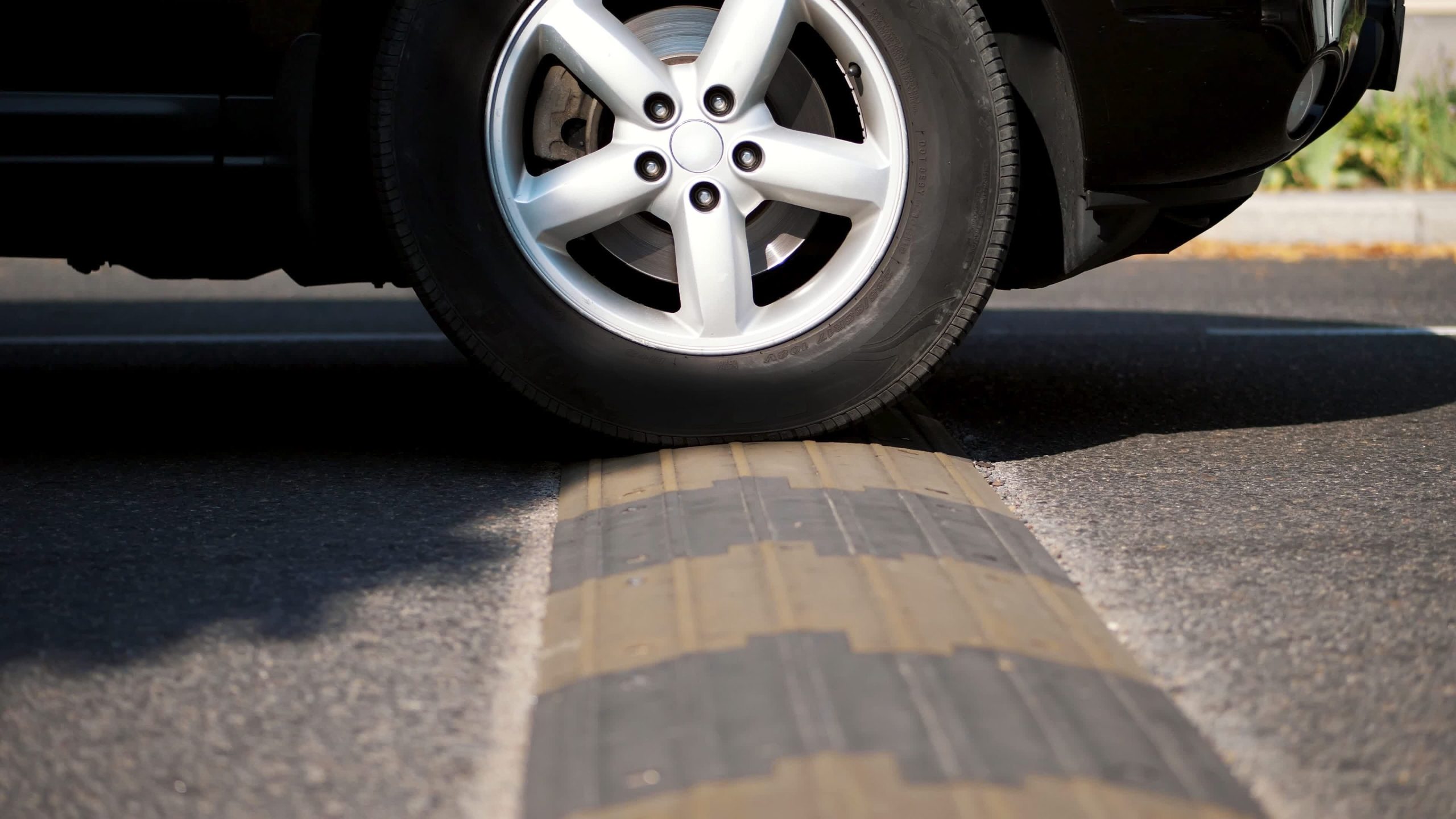 Close-up of a car tire rolling over a speed bump on a road, highlighting the tire's design and the textured surface of the bump.